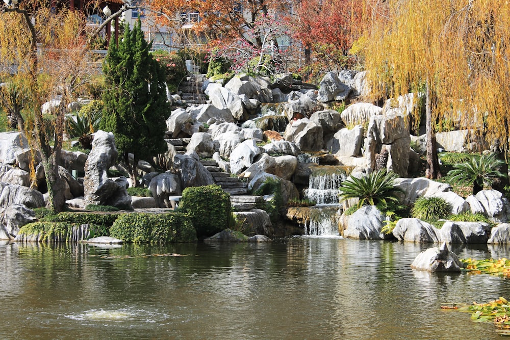 a pond with a waterfall surrounded by rocks and trees