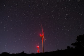 Night view of wind turbines illuminated by moonlight and stars.
