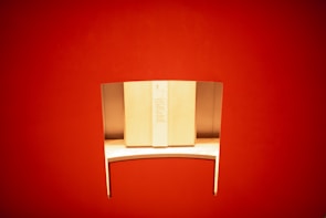 A sleek, minimalist wooden desk with a curved metal privacy divider is set against a vibrant red background. The desk is well-lit, highlighting its smooth surface and modern design.
