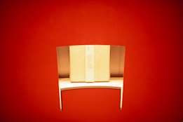 A sleek, minimalist wooden desk with a curved metal privacy divider is set against a vibrant red background. The desk is well-lit, highlighting its smooth surface and modern design.