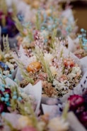 A collection of colorful dried flower bouquets featuring an assortment of different textures and colors. The arrangement includes pastel hues, with delicate buds and blooms that vary in shape and color. The bouquets appear carefully crafted, with some flowers slightly faded, enhancing their rustic charm.
