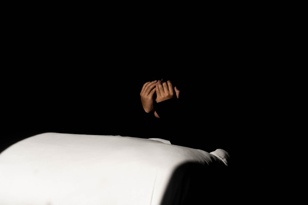 a person with their hands on a bed in the dark
