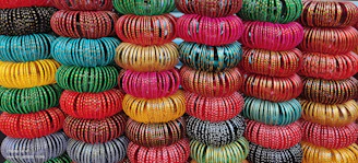 Close-up of colorful glass and metal bangles stacked neatly, reflecting warm gold and pink hues.