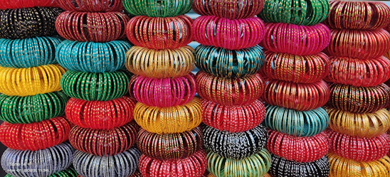 Close-up of colorful glass and metal bangles stacked neatly, reflecting warm gold and pink hues.