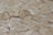 A close-up view of a surface covered in irregularly shaped, flat stone tiles. The stones are beige with visible cracks and subtle variations in color. The texture appears rough and weathered, indicating age or exposure to the elements.