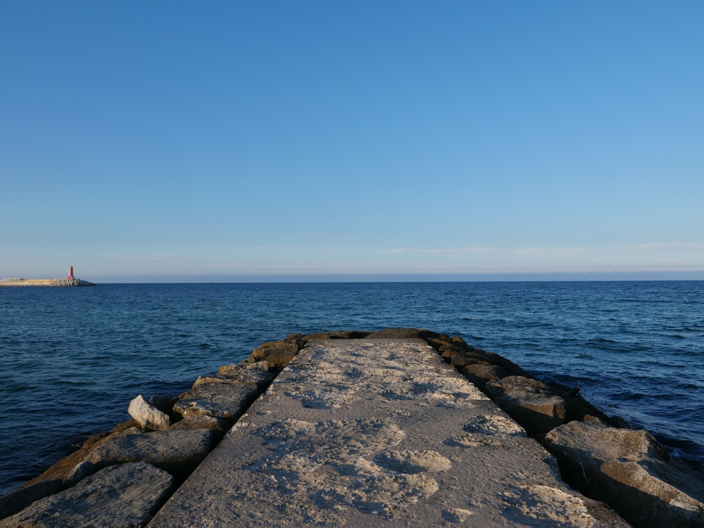 a stone pier with a lighthouse in the distance