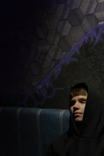 A moody, stylish black and red hoodie hanging against a dark textured wall.