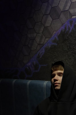 Black hoodie with subtle grey accents hanging against a textured dark wall.