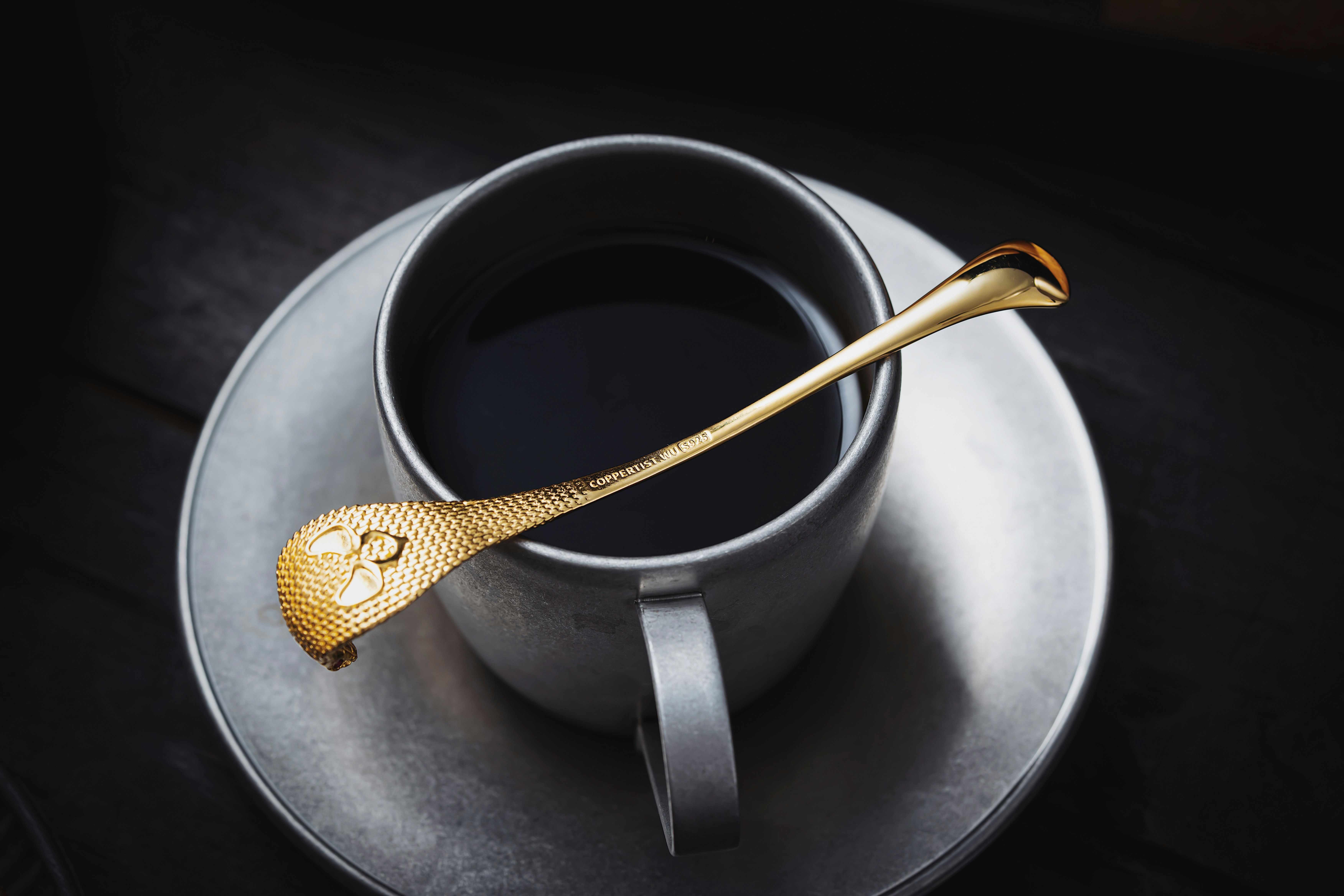 Black coffee in a grey cup with a gold spoon on the saucer