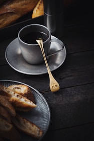 Artisan snacks beautifully plated alongside a steaming cup of coffee on a matte black table.