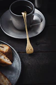 Elegant black tray holding a small coffee cup and a gold spoon, set against deep shadows.