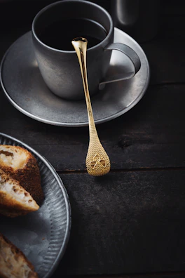 Elegant black tray holding a small coffee cup and a gold spoon, set against deep shadows.