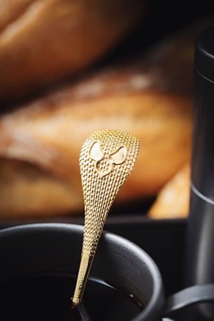 Close-up of a golden spoon stirring a warm beverage in a stylish espresso brown mug on a wooden table.