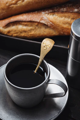 Personalized coffee cup with custom printing beside a matching gold spoon.