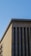 An angular view of a building with a modern architectural design featuring tall vertical windows and a flat roof. The facade is composed of beige stone and is set against a clear blue sky.