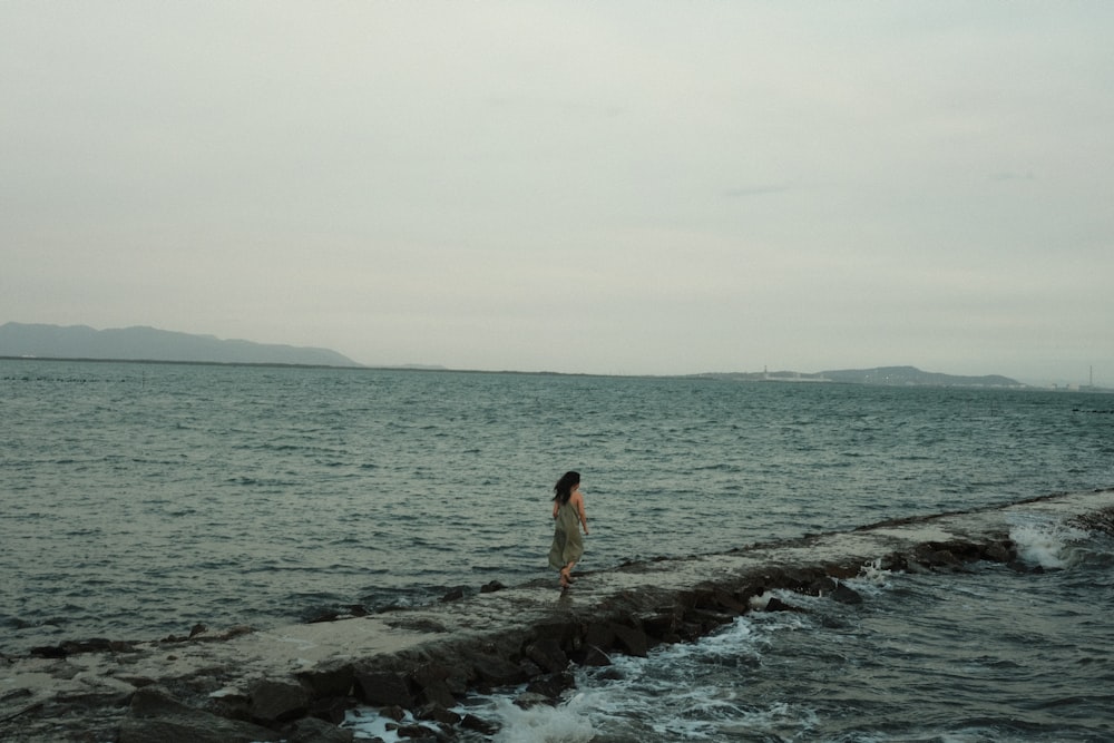 a woman standing on a rock wall next to the ocean