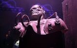 A dark, eerie setting featuring a menacing skeletal figure encased in a complex mechanical harness. The atmosphere is intensified by the presence of purple lightning in the background, and the scene is dimly lit, creating a sense of mystery and foreboding.