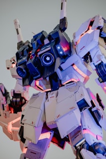 A large, detailed robot with a futuristic design, featuring armor plates and visible machinery elements. The structure includes glowing lights in blue and pink hues, adding a dynamic and high-tech aesthetic. The robot's scale suggests it's a life-sized model likely displayed outdoors or in a public area.