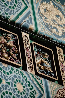 Intricate architectural details featuring ornate carvings of mythical creatures and abstract patterns, highlighted by gold accents and vibrant green hues. The prominent dragon motif is a central element, surrounded by floral designs that add depth to the composition.