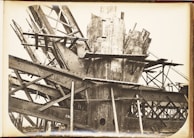 A complex structure of steel beams and riveted metal sheets arranged in an intricate, overlapping manner. The framework suggests an industrial or construction scene with a focus on heavy metalwork.
