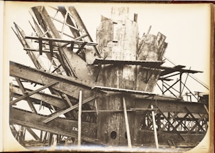 A complex structure of steel beams and riveted metal sheets arranged in an intricate, overlapping manner. The framework suggests an industrial or construction scene with a focus on heavy metalwork.