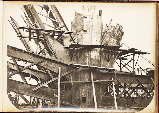 A complex structure of steel beams and riveted metal sheets arranged in an intricate, overlapping manner. The framework suggests an industrial or construction scene with a focus on heavy metalwork.