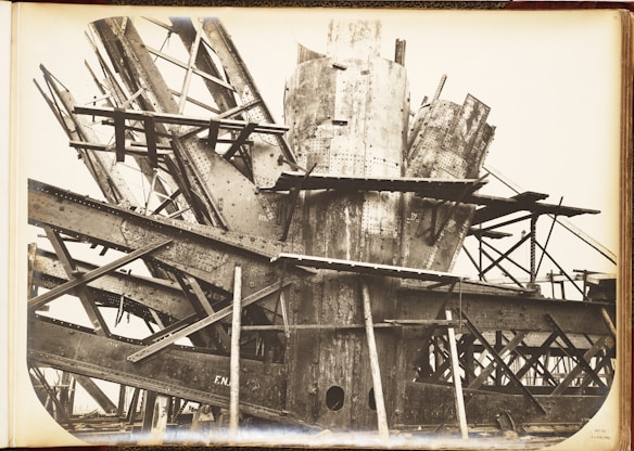 A complex structure of steel beams and riveted metal sheets arranged in an intricate, overlapping manner. The framework suggests an industrial or construction scene with a focus on heavy metalwork.
