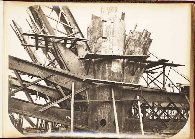 A complex structure of steel beams and riveted metal sheets arranged in an intricate, overlapping manner. The framework suggests an industrial or construction scene with a focus on heavy metalwork.