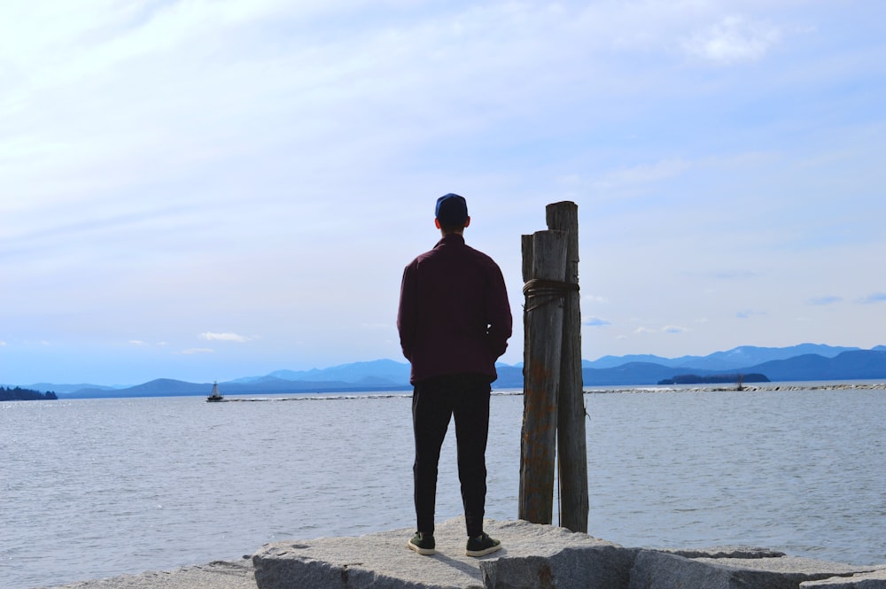 a man standing on top of a rock next to a body of water