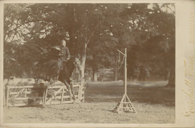 A rider gracefully jumping over a rustic wooden fence during a sunny day event.