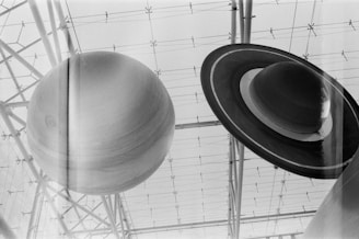 Large spherical models resembling planets are suspended from the ceiling. The structures are framed by a grid-like structure that appears to belong to a planetarium or museum. The image is in black and white, giving it a classic and timeless feel.