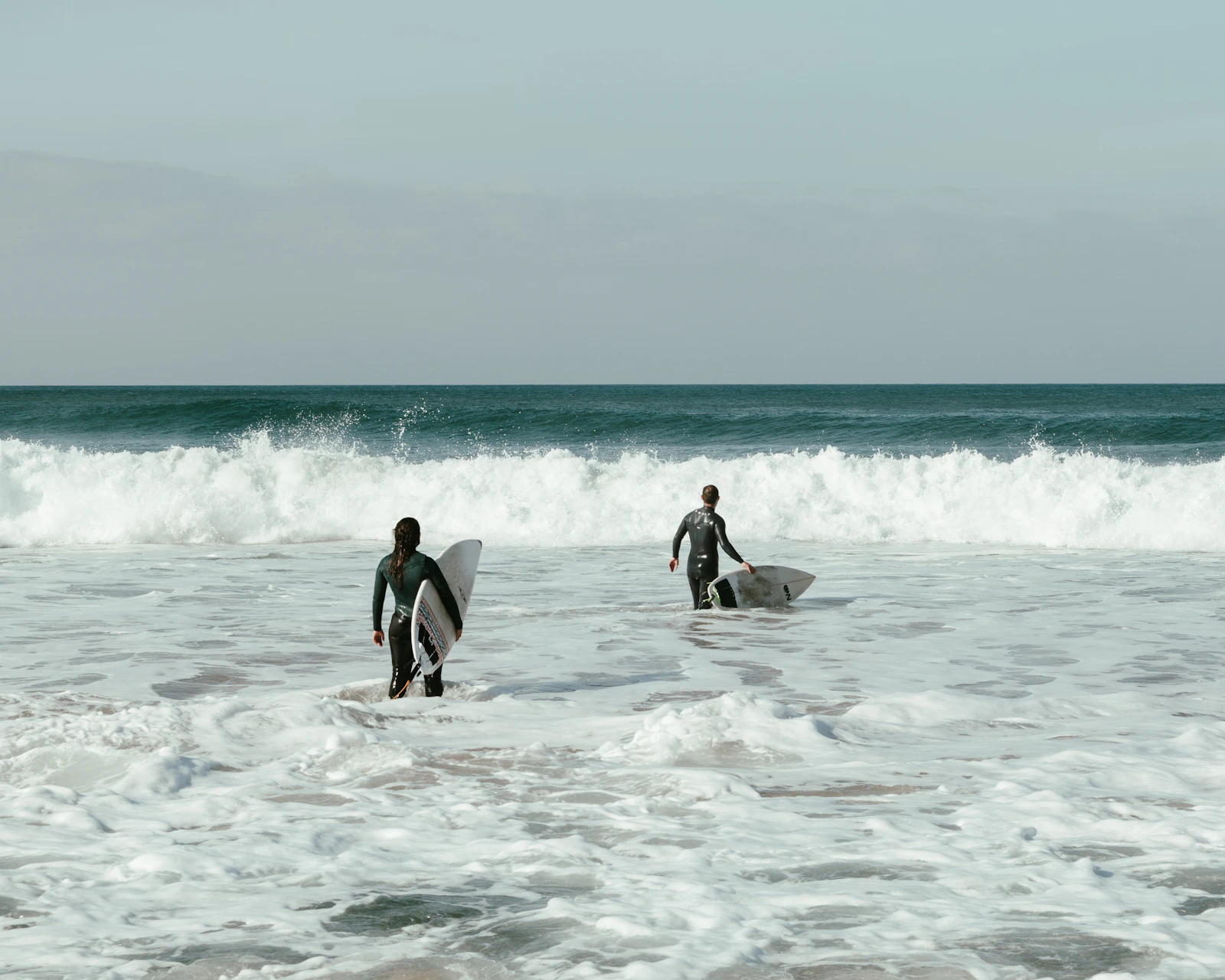 Two surfers walking into the ocean in Ericeira, Portugal