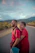 Smiling tourist couple standing beside a parvatyatra cab on a scenic mountain road.