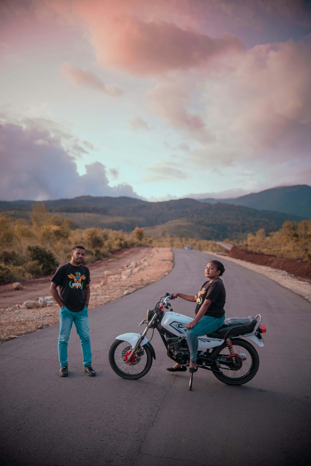 two men standing next to a motorcycle on a road
