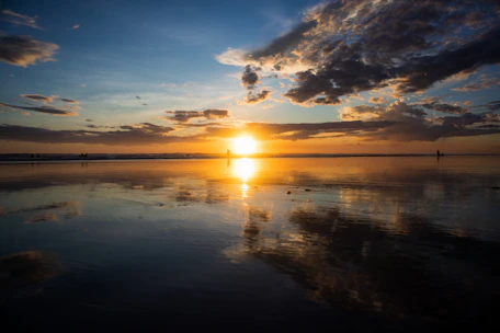 A stunning sunset view over a calm beach with a couple enjoying the moment.