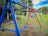 Children laughing and swinging joyfully on colorful playground swings under a bright sky.