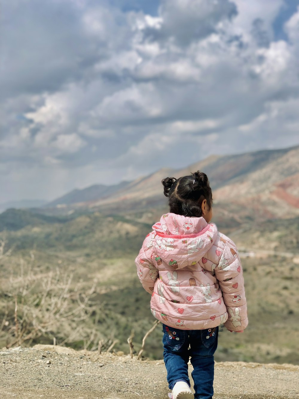 a little girl in a pink jacket walking down a hill