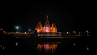 A serene nighttime view of Shri Khatu Shyam Mandir illuminated in golden light against a deep black sky.