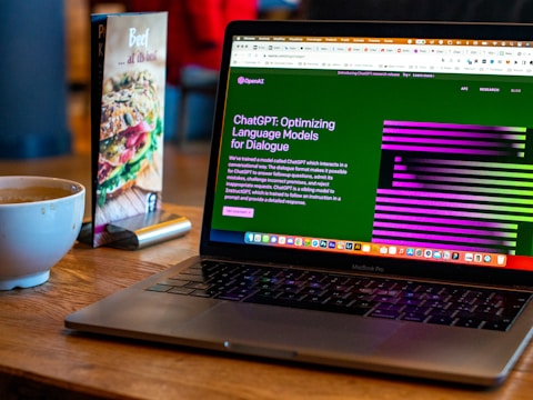 A laptop displaying a website about language models is set on a wooden table. A coffee cup is nearby, next to a menu stand featuring a beef dish advertisement.