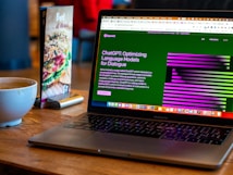 A laptop displaying a website about language models is set on a wooden table. A coffee cup is nearby, next to a menu stand featuring a beef dish advertisement.