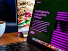 A laptop displays a screen with the title 'ChatGPT: Optimizing Language Models for Dialogue', accompanied by descriptive text. The background shows a blurred image of a sandwich, and there's a white cup on the wooden table next to the laptop.