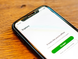 A smartphone with a cracked screen displays a message indicating that it is offline with options to try again or read help articles. The device is resting on a wooden surface.