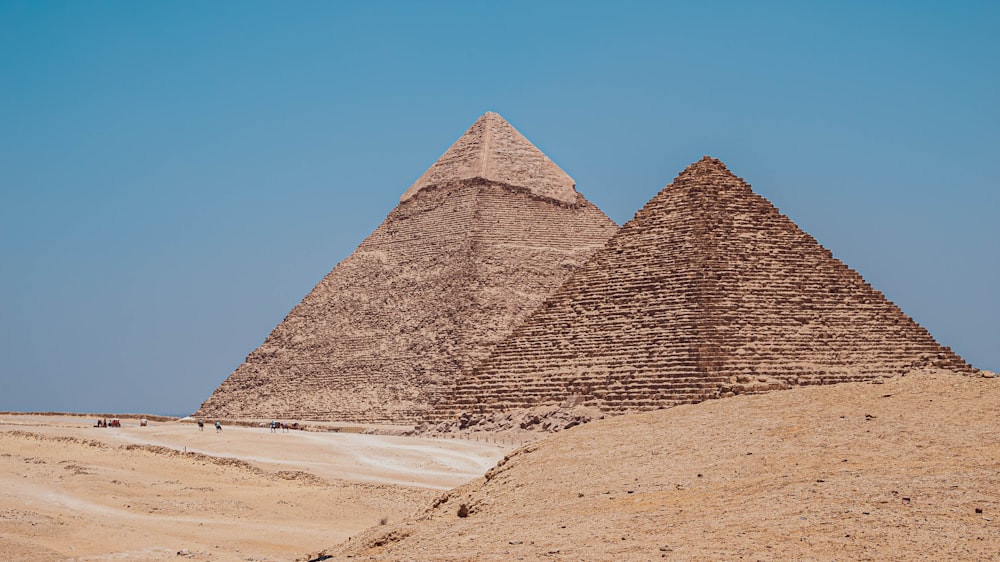 duas pirâmides no deserto com um céu azul no fundo