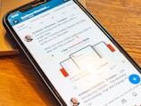 A smartphone displaying a social media post featuring a text discussing transformation and steps to take with a product. The phone is placed on a wooden desk, and there is a partial view of a laptop nearby.