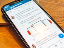 A smartphone displaying a social media post featuring a text discussing transformation and steps to take with a product. The phone is placed on a wooden desk, and there is a partial view of a laptop nearby.