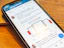 A smartphone displaying a social media post featuring a text discussing transformation and steps to take with a product. The phone is placed on a wooden desk, and there is a partial view of a laptop nearby.