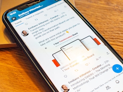 A smartphone displaying a social media post featuring a text discussing transformation and steps to take with a product. The phone is placed on a wooden desk, and there is a partial view of a laptop nearby.