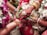 A close-up view of a wedding ritual where two hands are joined together. The bride's hand is adorned with intricate henna designs, gold bracelets, and rings. She holds betel leaves. There are flower garlands in the background, and the atmosphere is colorful and festive.
