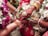 A close-up view of a wedding ritual where two hands are joined together. The bride's hand is adorned with intricate henna designs, gold bracelets, and rings. She holds betel leaves. There are flower garlands in the background, and the atmosphere is colorful and festive.