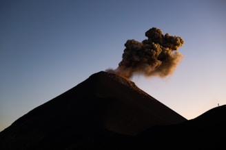 A dramatic shot of an active volcano with smoke rising against a sunset sky